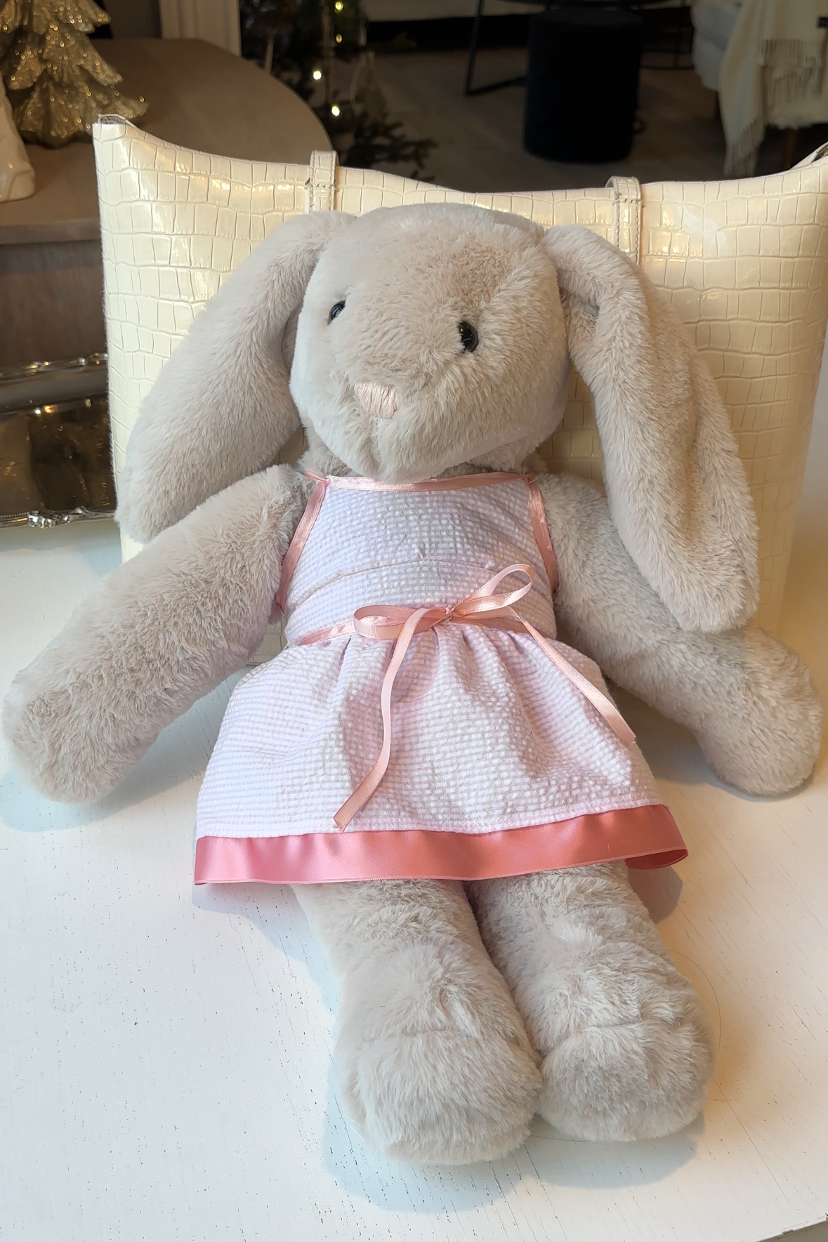 Stuffed animal in a red dress sitting on a white surface with a blurred indoor background. Plushie plush bunny sewing pattern tutorial, making build-a-bear, diy plushie, diy bunny, making toy toys, build-a-bear clothes, homemade Christmas gift, tiktok sewing pattern, homemade toy, homemade plushie, plushie pattern, bunny pattern, birthday gift child, birthday gift girl 6yo